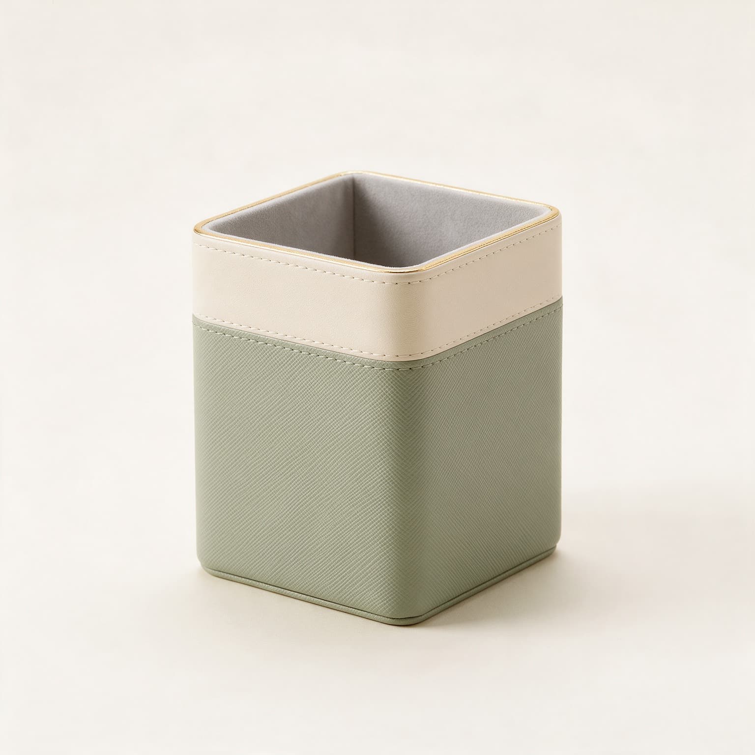Square desk tidy in sage green textured faux leather with a cream upper band, gold trim and a grey velvet lining