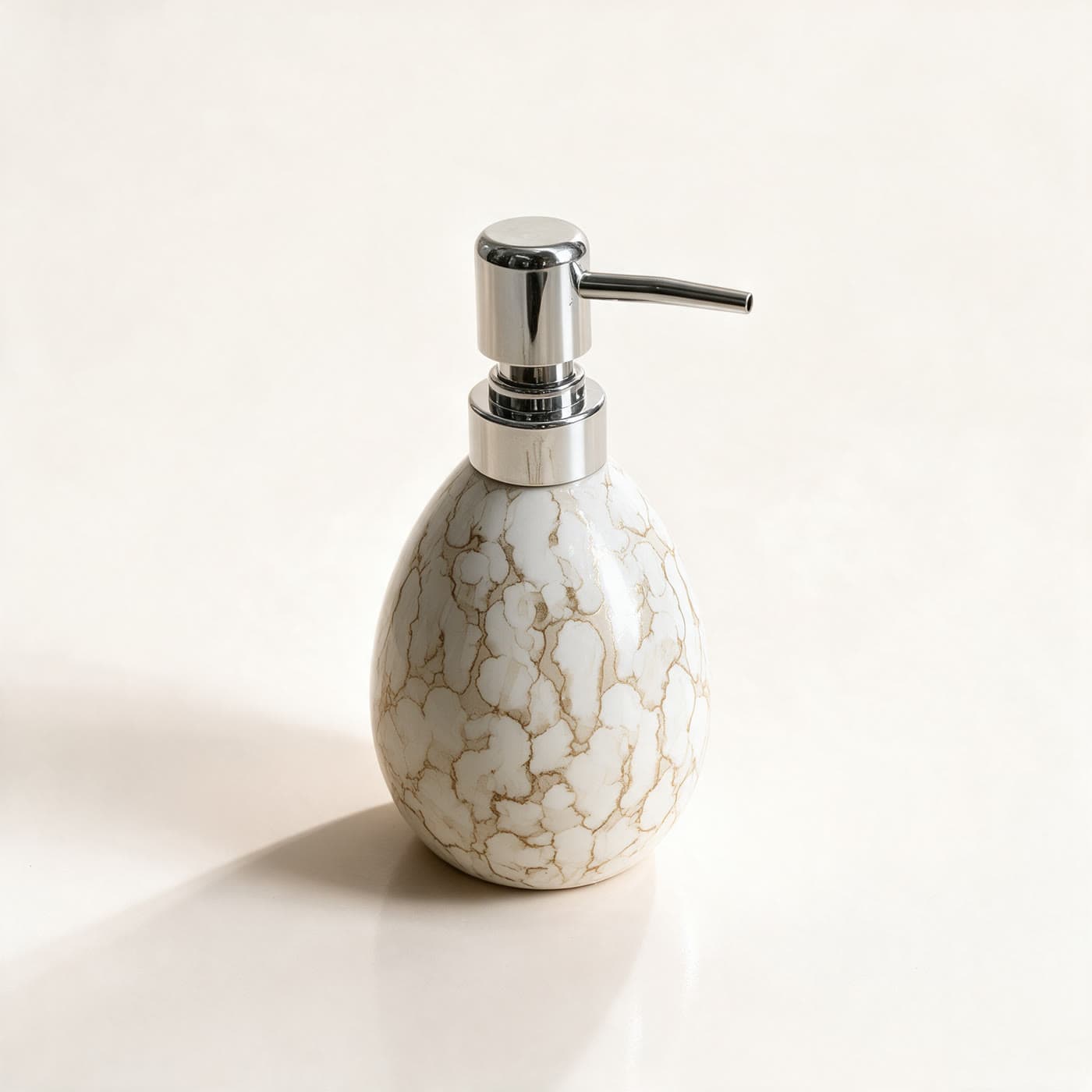 Rounded ceramic soap dispenser in glossy ivory with antique-gold crackle marbling and a polished chrome pump, on a warm off-white background
