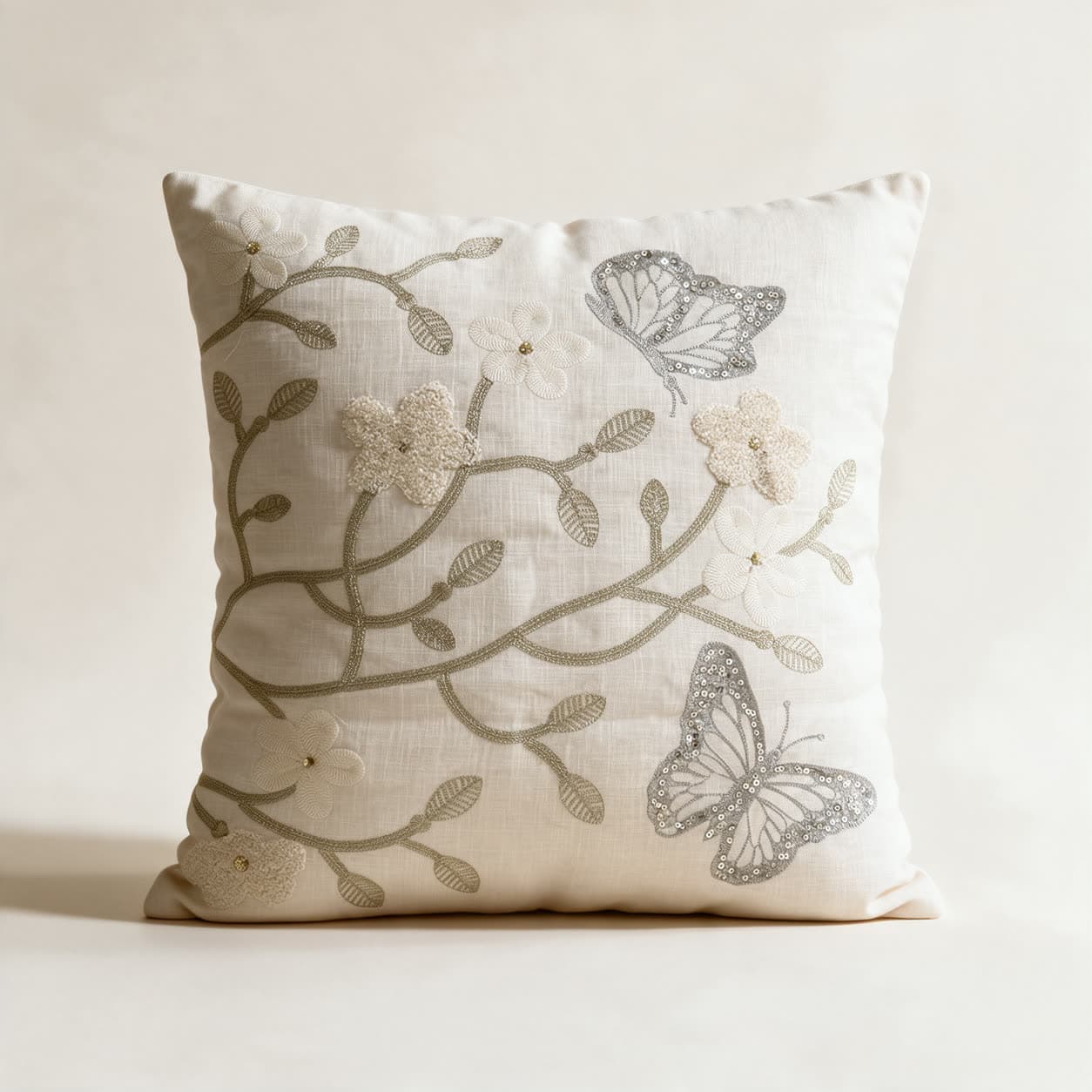 Ivory linen cushion cover hand-embroidered tone on tone with a pale gold vine, cream flowers and two silver sequinned butterflies, on a warm off-white background