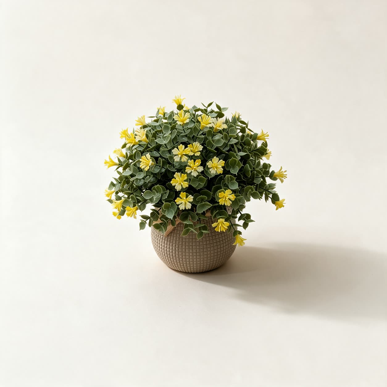 Small artificial flowering bush with yellow flowers and round green leaves in a textured greige ceramic pot, on a warm off-white background