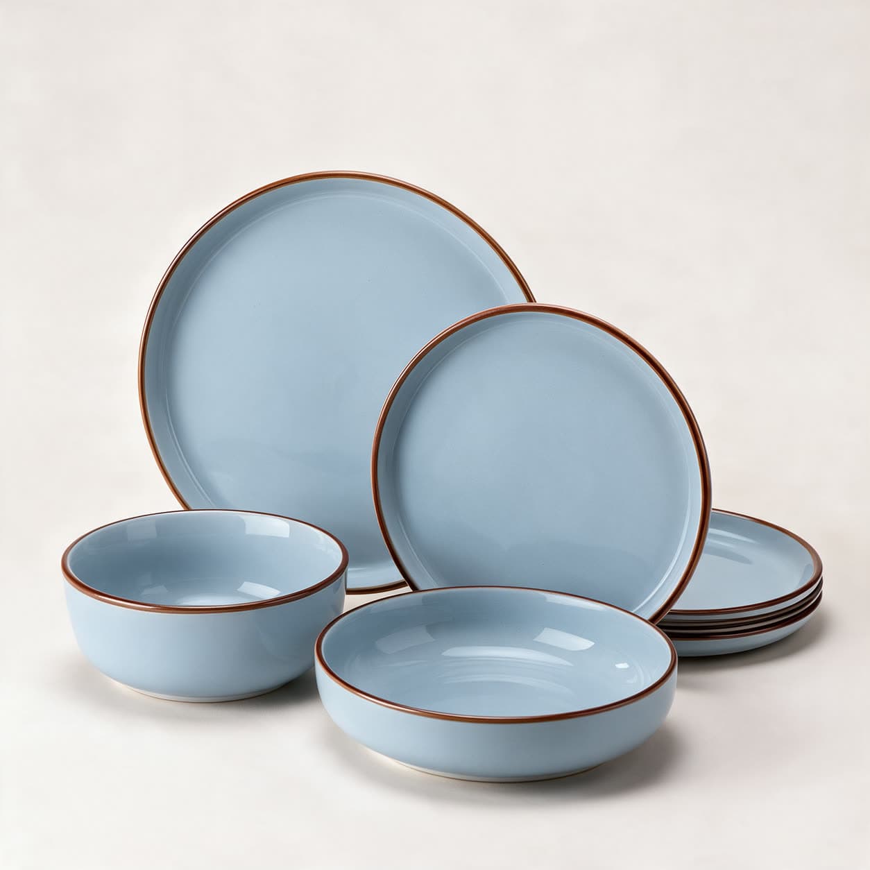 Powder blue stoneware dinner set edged with a fine russet-brown rim line — dinner plate, side plate, pasta bowl, cereal bowl and a stack of plates — on a warm off-white background