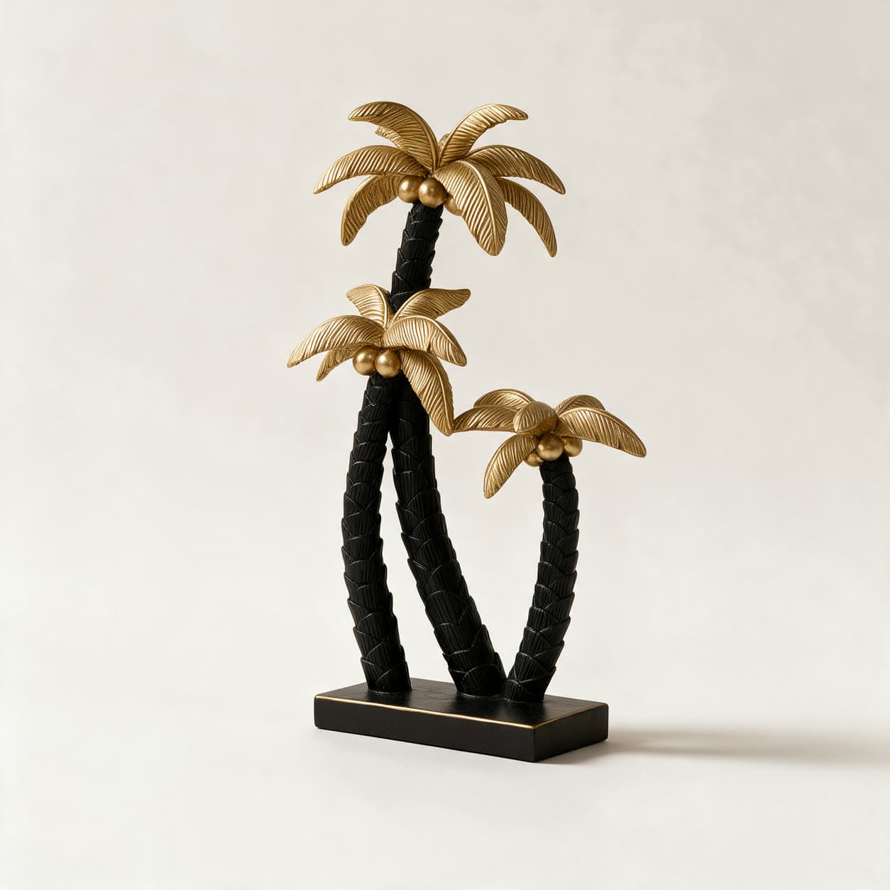 Cast resin sculpture of three curved palm trees with matte black woven trunks and gold fronds on a black rectangular base, on a warm off-white background