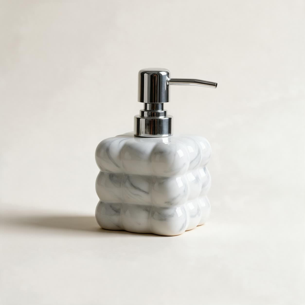 Square cloud-shaped soap dispenser in grey and white marbled ceramic with a chrome pump, on a warm off-white background