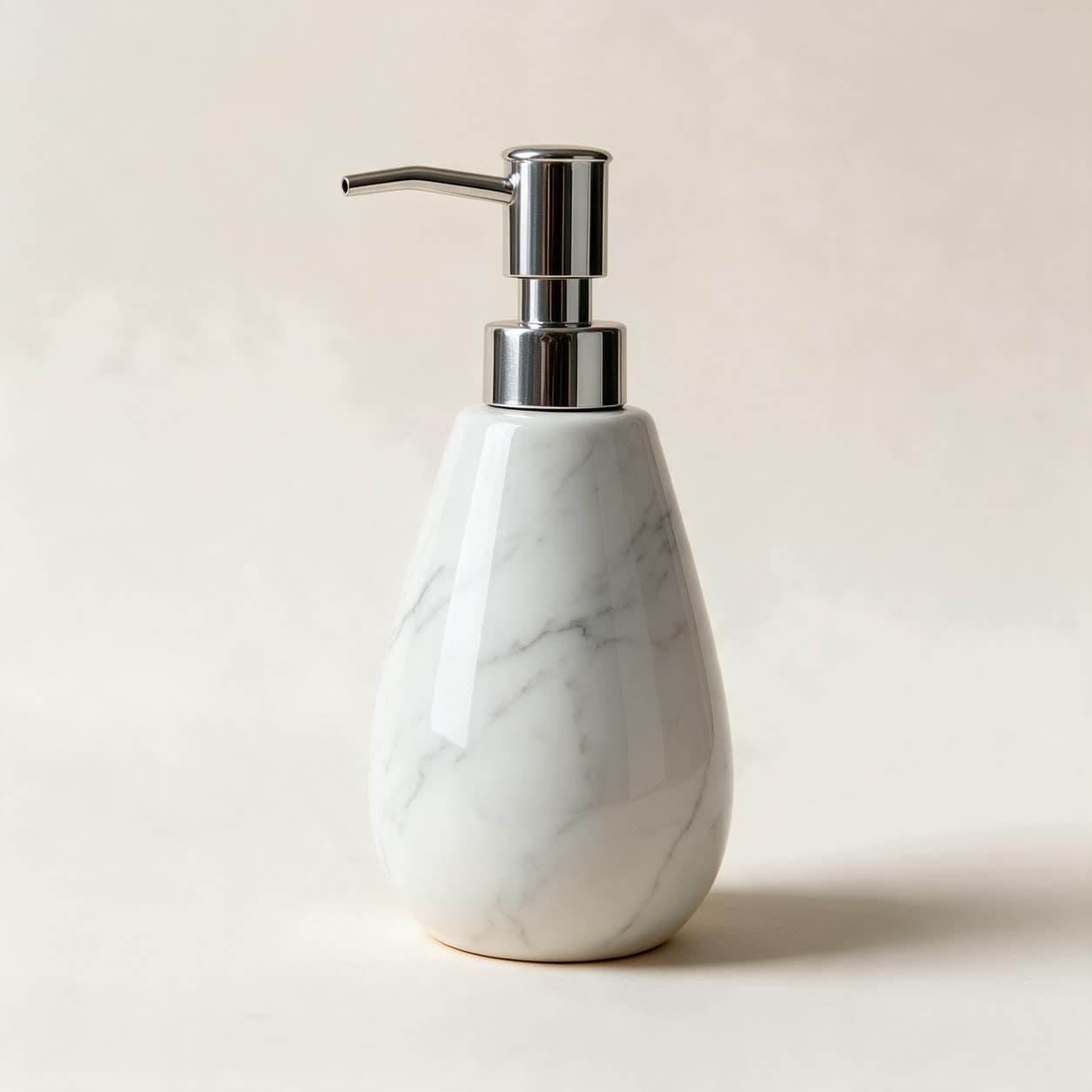 Teardrop-shaped soap dispenser in white ceramic with fine grey marble veining and a chrome pump, on a warm off-white background