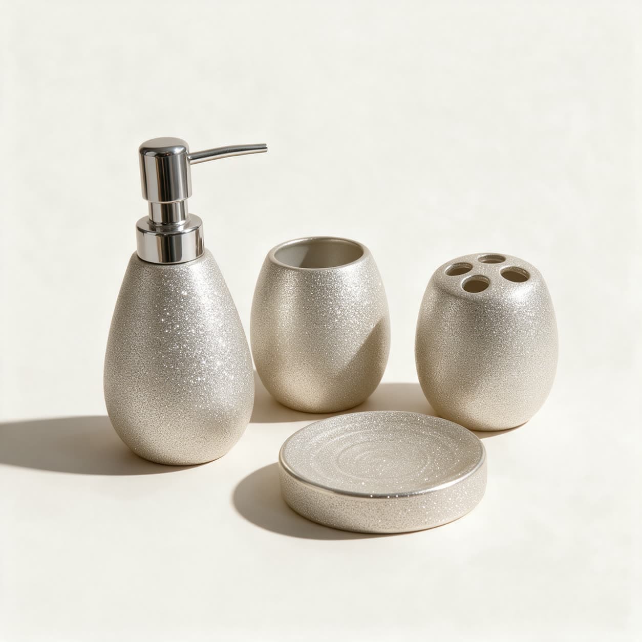 Four-piece bathroom set in textured champagne silver — a teardrop soap dispenser, an egg-shaped tumbler, a toothbrush holder with five holes and a round soap dish — on a warm off-white background