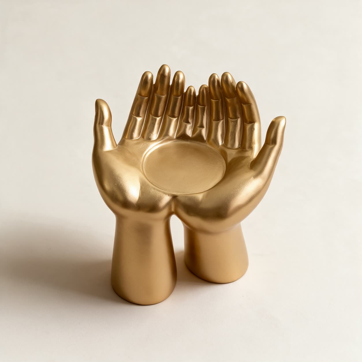 Satin gold cast resin trinket dish shaped as a pair of open cupped hands raised on their wrists, on a warm off-white background