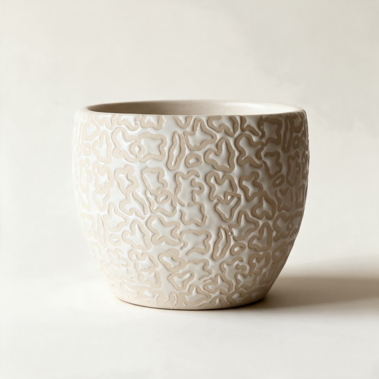 Rounded ceramic planter covered in a raised maze-like relief of bare sandy clay with thick glossy cream-white glaze pooling between the lines, on a warm off-white background