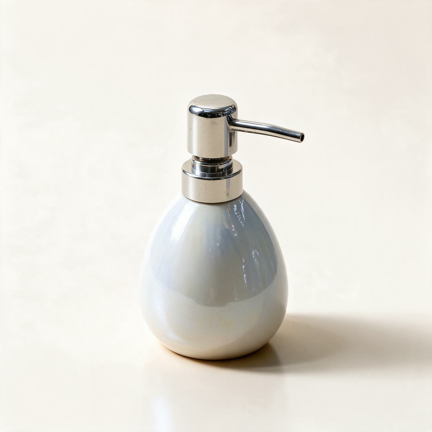 Rounded ceramic soap dispenser in pearlescent opal white with a soft blue shimmer and a polished chrome pump, on a warm off-white background