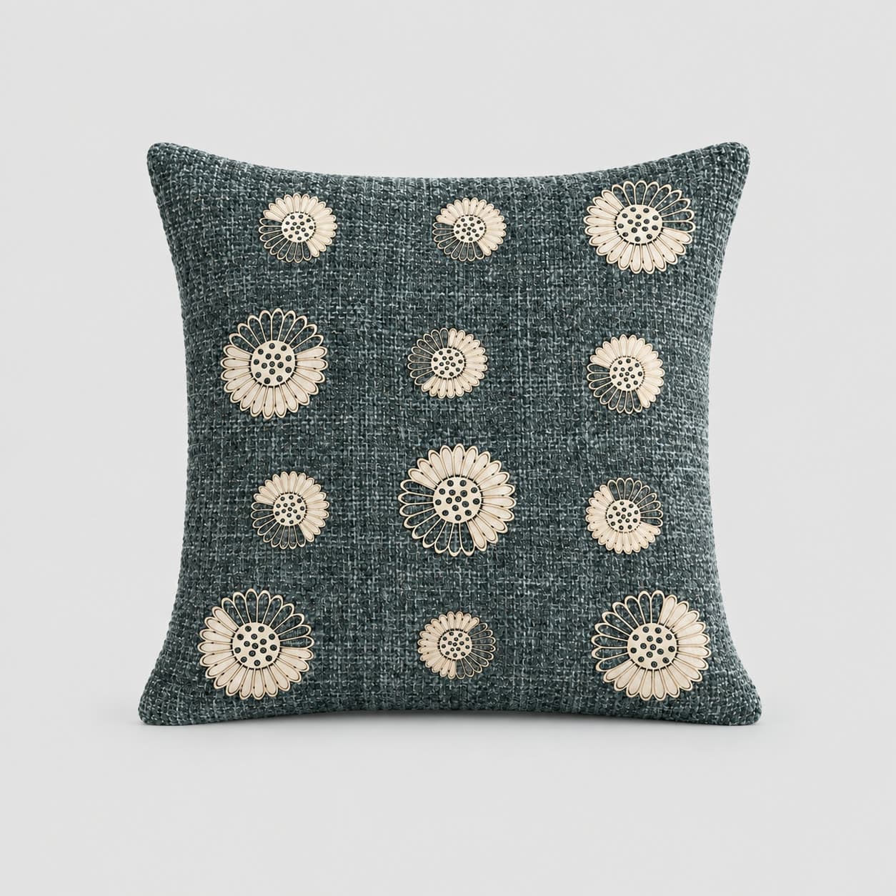 Deep slate-teal cushion cover in a chunky slubby weave, scattered with cream appliqué medallions, on a pale grey background