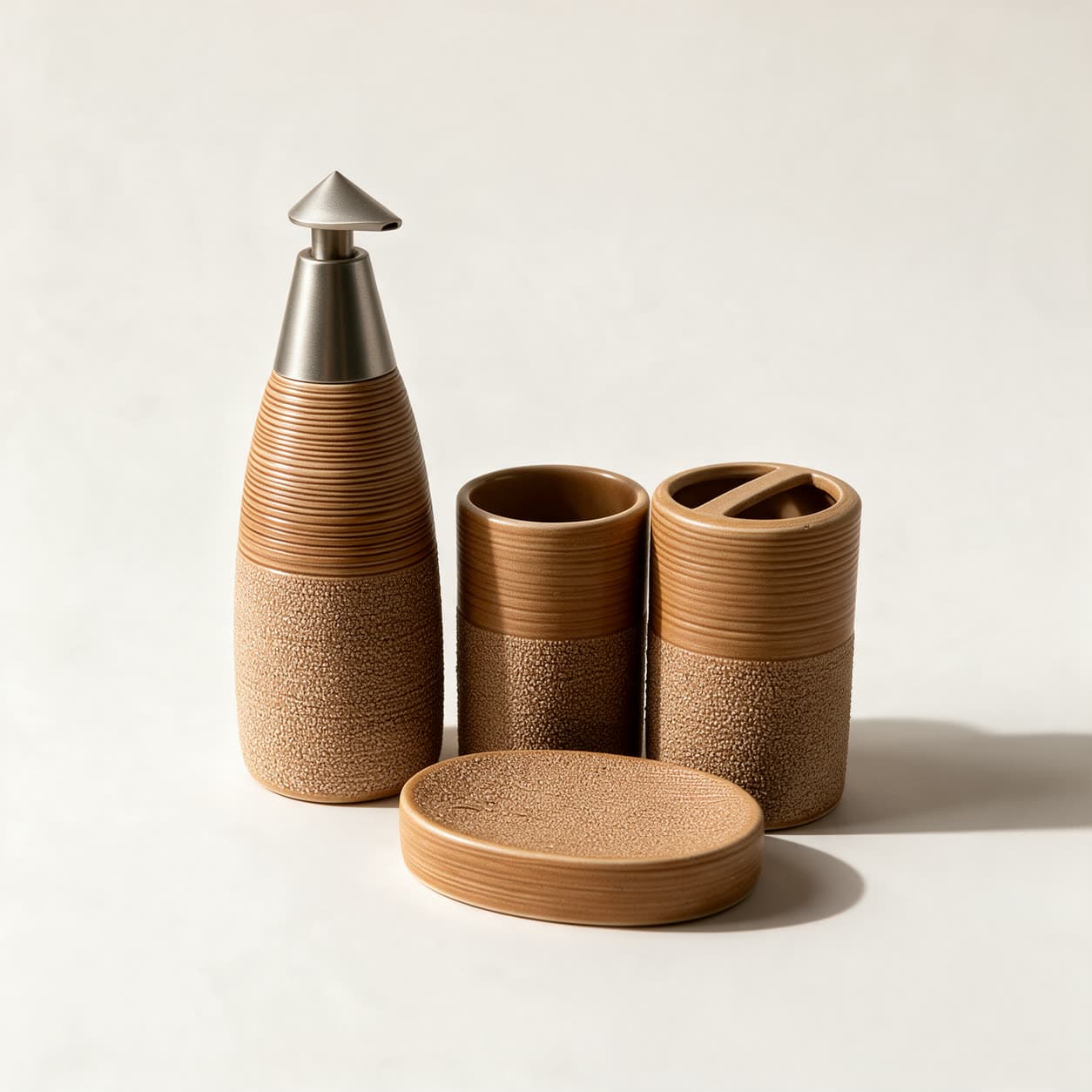 Four-piece terracotta tan bathroom set — a tall ribbed bottle dispenser with a pointed silver pump, a tumbler, a toothbrush holder and a round soap dish — on a warm off-white background