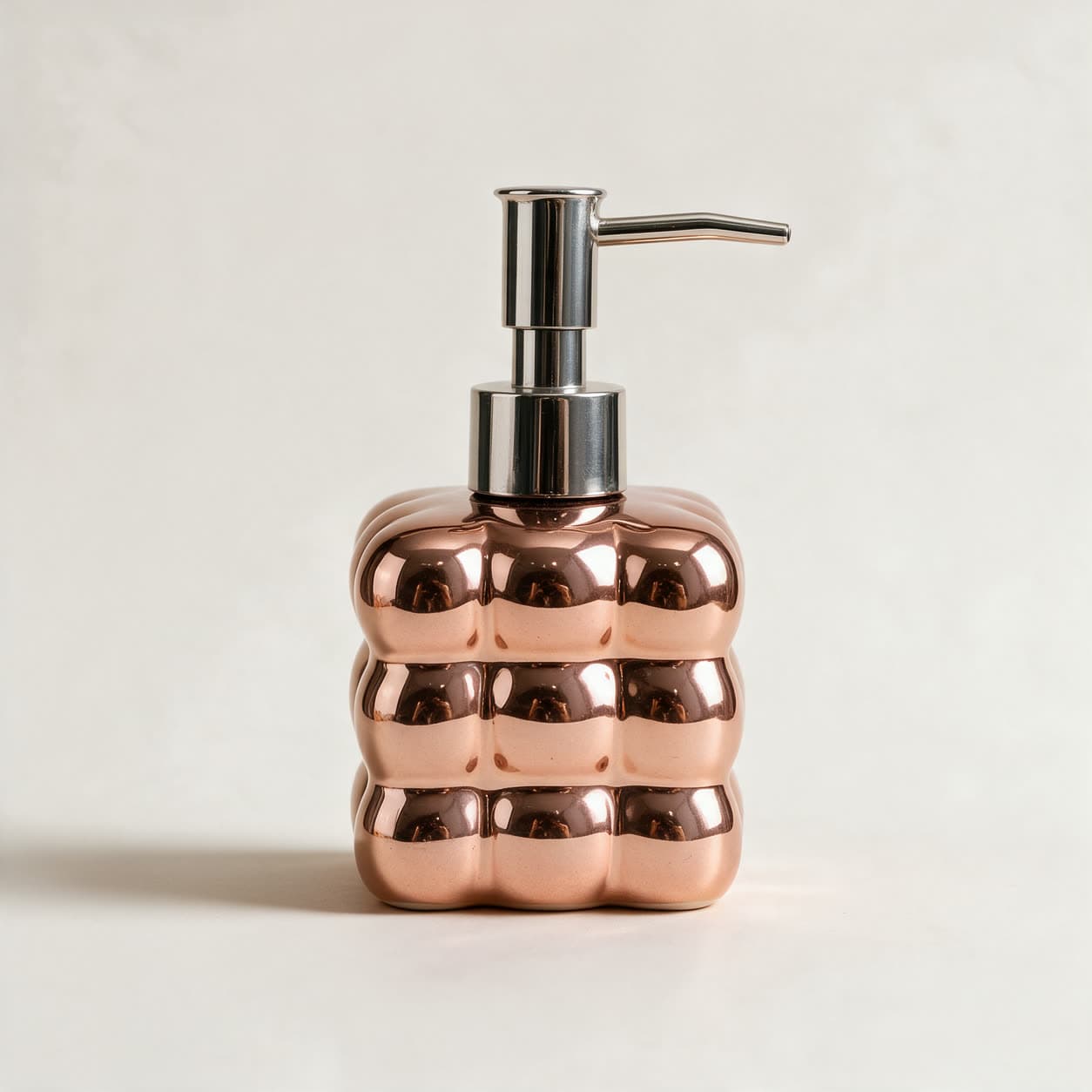Square cloud-shaped soap dispenser in mirror-bright rose gold with a chrome pump, on a warm off-white background